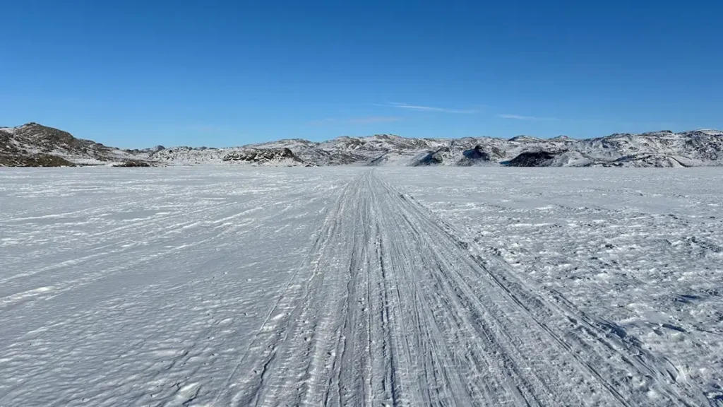 Vyjeté stopy vedoucí do dálky přes rozlehlou zasněženou pláň na trase Arctic Circle Trail, které dokonale ilustrují arktickou samotu a rozlehlost Grónska.